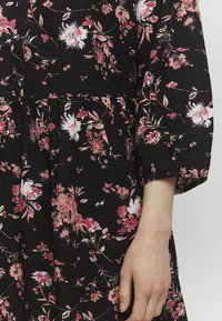 Abito nero a fiori con vita arricciata, maniche lunghe e un mix di motivi floreali rosa e bianchi. Chiusura con bottoni sul davanti e tessuto morbido.