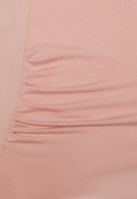 Tecido rosa com uma textura suave apresenta franzidos laterais para um detalhe extra. O material parece elástico e leve.