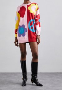 Maglione oversize colorato in rosa, rosso e giallo con motivi a fiori e cuori. Abbinato a stivali neri in pelle al ginocchio.