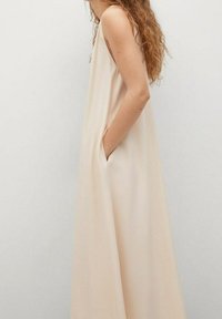 Lange, mouwloze jurk van lichtbeige stof. Heeft zijzakken, een ontspannen silhouet en een gladde textuur, met minimale details.