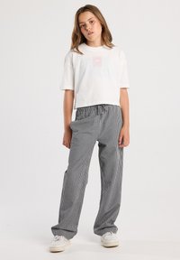 White cropped t-shirt with a pink graphic on the chest, paired with black and white checkered loose-fitting pants. White sneakers complete the look.