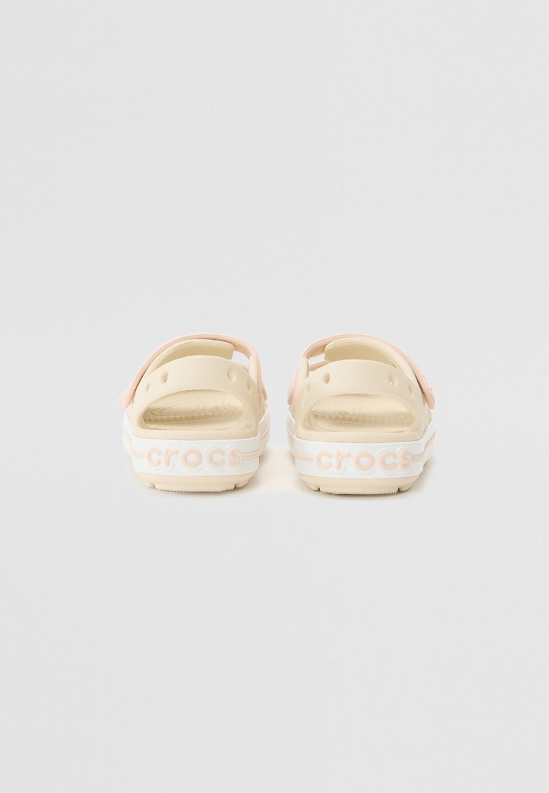 Vista posteriore di sandali Crocs beige con accenti rosa, caratterizzati da un design perforato, branding testuale e una soletta texture per il comfort.