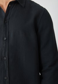 Schwarzes Hemd mit Knopfleiste aus leichtem Stoff mit weicher Textur, ausgestattet mit einem klassischen Kragen und sechs vorderen Knöpfen.