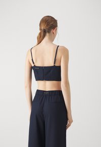 Navy cropped top dengan tali tipis yang dapat disesuaikan dan penutupan resleting belakang. Dipadukan dengan celana navy berkualitas tinggi dengan pinggang tinggi yang memiliki saku samping.