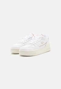 Hvit sneakers med en strukturt lær overdel, tykk kremfarget såle, og subtile logo-detaler i en lys ferskenfarge på hælen og tungen.