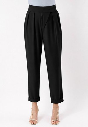 Pantaloni neri a vita alta con gamba affusolata, pieghe e risvolti, indossati con sandali beige con cinturini e tacco alto e una maglietta azzurro chiaro.