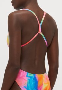 Maillot de bain multicolore avec un motif tourbillonnant. Dispose de fines bretelles croisées en rose et vert, fabriquées à partir d'un tissu lisse et extensible.