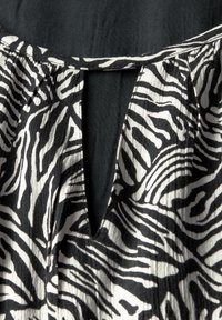 Schwarz-weißes Gewebe mit einem Zebramuster, das ein Schlüssel-ausschnitt Detail am Ausschnitt und eine strukturierte Oberfläche aufweist.