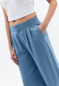 Lichtblauwe geplooide broek gemaakt van een gladde stof, met een hoge taille en zijzakken.