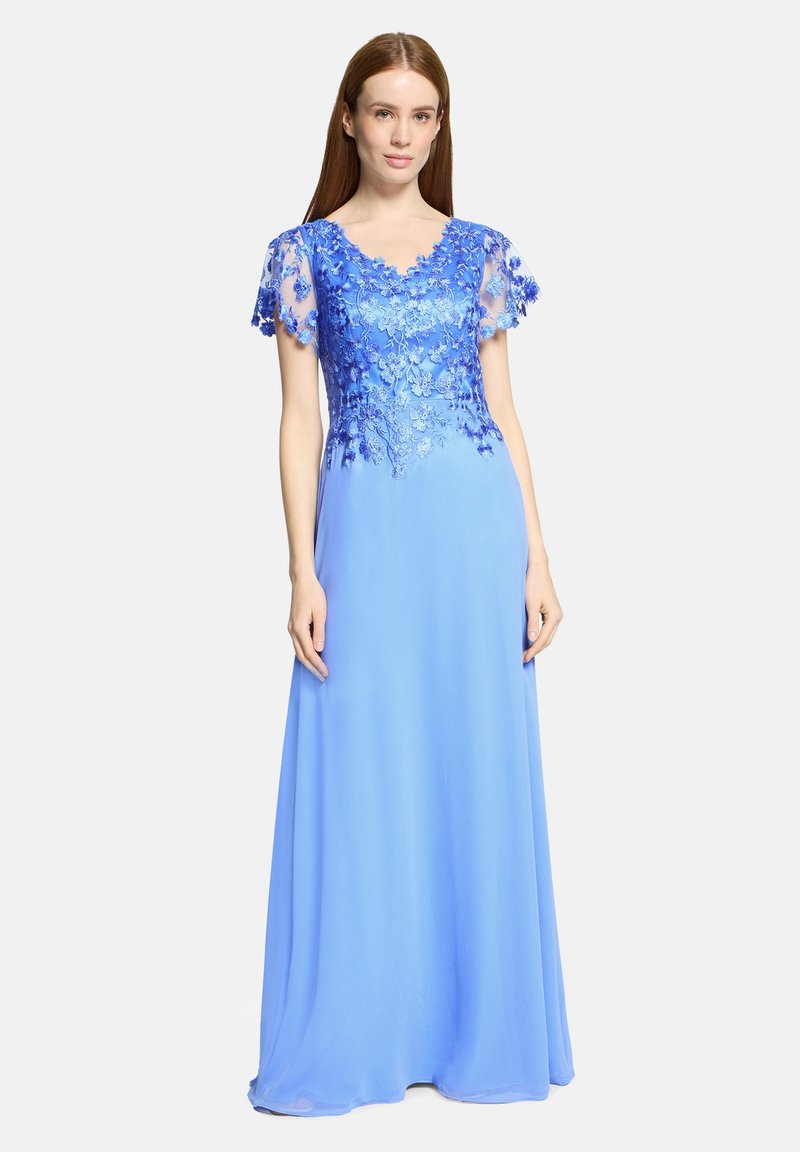 Frau trägt ein bodenlanges, hellblaues Kleid mit transparenten kurzen Ärmeln und detaillierter Blumenstickerei auf dem Oberteil und den Ärmeln.