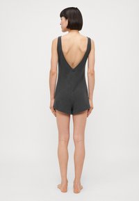 Romper gris oscuro con un profundo escote en la espalda en V, tirantes anchos y piernas cortas. Textura suave y diseño casual adecuado para llevar de forma relajada.