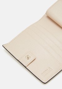 Světle béžové kožené peněženky uvnitř s texturovaným povrchem, která obsahuje více přihrádek na karty a detail s upevněním na cvok. Jemné logo vytlačené.