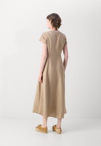 Beige, knee-length dress with short sleeves, relaxed fit, and soft texture. Paired with light brown shoes featuring fuzzy accents.