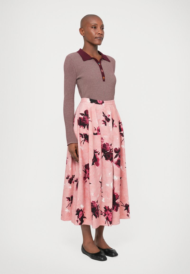 Grå långärmad ribbad polo med vinröd krage och knappar, kombinerad med en rosa blommig kjol. Svarta platta skor fulländar outfiten.