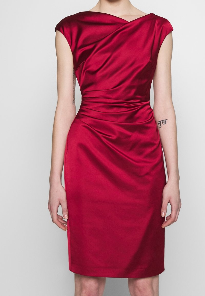 Robe en satin rouge avec manches courtes, corsage drapé et taille froncée. Longueur au genou, texture lisse et légère brillance.