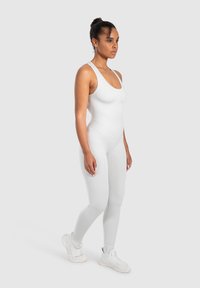 Bodysuit ajustado blanco hecho de material elástico, con un escote redondeado y tirantes delgados, combinado con zapatillas deportivas blancas.