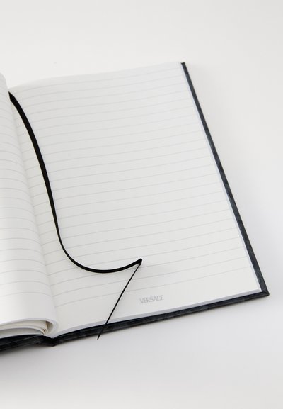 Taccuino a copertina rigida nera con pagine a righe, caratterizzato da un segnalibro a nastro nero e dal marchio Versace nell'angolo in basso a destra.
