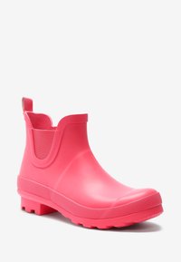 Botte de pluie en caoutchouc rose vif à la cheville avec languette, semelle texturée et goussets élastiques sur les côtés pour un enfilage facile.