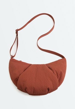 Hnedá textúrovaná látková crossbody taška s oblým, polstrovaným dizajnom a nastaviteľným ramenným popruhom na bielom pozadí.