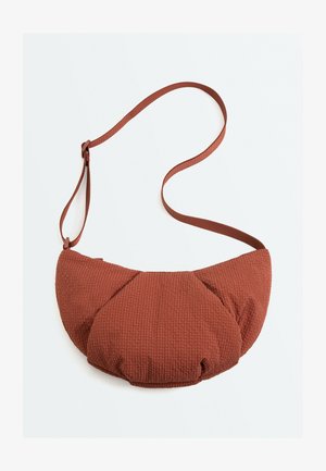 Hnedá textúrovaná látková crossbody taška s oblým, polstrovaným dizajnom a nastaviteľným ramenným popruhom na bielom pozadí.