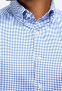 Košile na knoflíky v světle modrém a bílém kostkovaném vzoru, vybavená límečkem, bílými knoflíky a hladkou texturou látky.