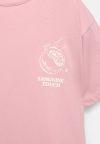 Pink t-shirt med en hvid linjetegning af et granatæble og teksten "SANGUINE TOUCH" trykt under grafikken på brystet.