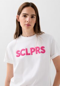 Bílý bavlněný tričko s výraznými růžovými vyšívanými písmeny "SCLPRS". Krátké rukávy s detaily na manžetách. Jednoduchý a čistý design.