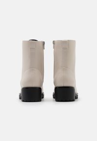 Stivali alla caviglia beige in pelle liscia con punta arrotondata, suole in gomma nera e dettaglio con zip laterale. Design semplice ed elegante.