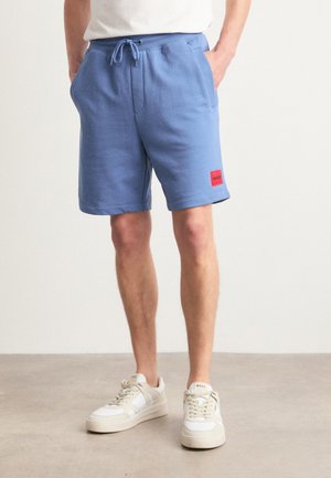 Shorts en coton bleu avec une taille élastique et un cordon de serrage. Comprend des poches latérales et une étiquette de logo rouge sur la jambe gauche.