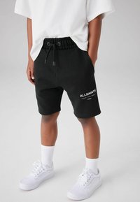 Svarta bomullsshorts med resårmidja och dragsnöre, med "ALLSAINTS"-logotypen i vitt. Matchade med vita sneakers och strumpor.