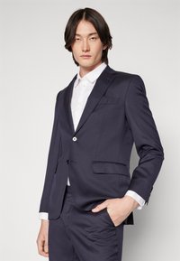 Navy blazer and trousers set in smooth fabric, featuring a single button, notch lapels, and front patch pockets, paired with a white shirt.