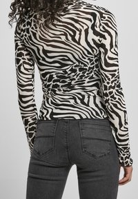 Långärmad topp i zebramönster, tillverkad av mjukt tyg, med en figurnära design. Kombinerad med grå denimjeans.