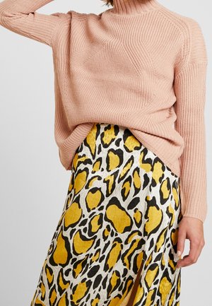 Femme portant un pull en maille rose clair rentré dans une jupe imprimée animal jaune, noire et blanche avec une fente à l'avant.