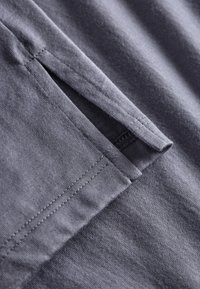 Close-up van charcoal grijze stof die een netjes gestikte zakopening toont met scherpe randen en een gladde textuur.