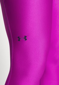 Leggings atletici viola realizzati in materiale liscio e elasticizzato con accenti neri del logo. Caratteristiche includono un design aderente e una texture elegante.