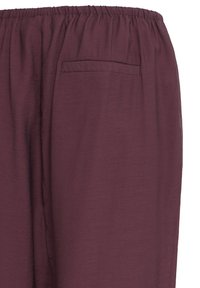Pantalon à taille élastique marron avec une seule poche arrière, fabriqué en tissu léger et texturé.