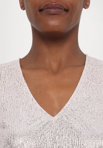 V-neck top in soft pink fabric with a textured surface embellished with reflective sequins. Smooth neckline and subtle shine.