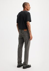 Grå denimjeans med rett snitt, lærpatch bak i midjen, og svart kortermet t-skjorte, sett fra baksiden.