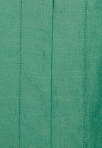 Texturovaná tyrkysová látka s vertikálními švy; hladký povrch s mírným leskem. Vhodná pro oděvy nebo čalounění.