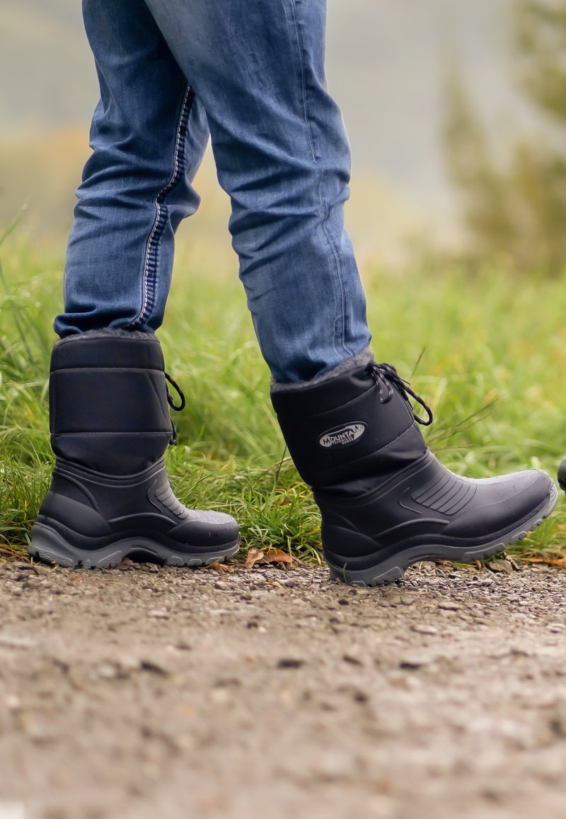 Zwarte geïsoleerde laarzen met een textuur, vetersluiting en een gevoerde kraag. Ze hebben een stevige rubberen zool en worden gedragen met een blauwe spijkerbroek.