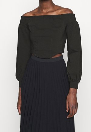 Toppi, joka on lyhennetty ja olkaimeton musta, jolla on pitkät puffi-hihat ja sauman yksityiskohtia, yhdistettynä pleated tummansiniseen hameeseen.