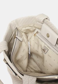 Grande borsa intrecciata beige con un interno liscio, tasca con zip e foderatura brandizzata che presenta piccoli loghi ripetuti e motivi triangolari.