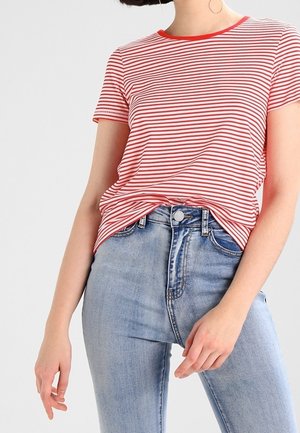 Krótki rękaw koszulki w czerwono-białe paski z okrągłym dekoltem, noszona na jasnoniebieskich, wysokich dżinsach z detalem guzika i kieszeni.