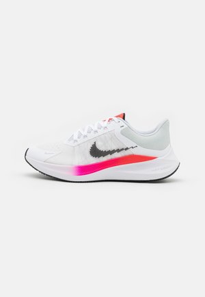 Zapatilla de correr blanca de Nike con el logo negro, entresuela degradada en rosa, cordones blancos y cuello de talón acolchado gris sobre fondo blanco.