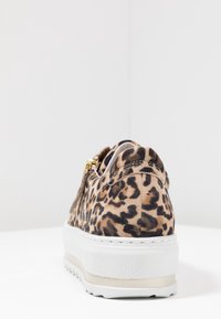 Des chaussures slip-on en suède à motif léopard, avec une semelle en caoutchouc texturé blanc et un accent de fermeture éclair doré sur le côté.