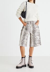 Maglione spesso lavorato a maglia crema, pantaloni shorts in stampa serpente nelle tonalità del grigio e stivaletti militari beige con suola e lacci neri. Piccola borsa a tracolla nera.