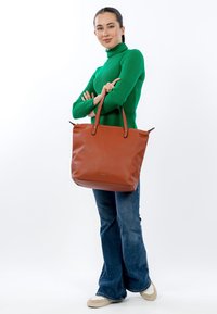 Brown leather tote bag with two handle straps and a soft texture. Worn with blue flared jeans and cream sneakers. Green ribbed sweater.