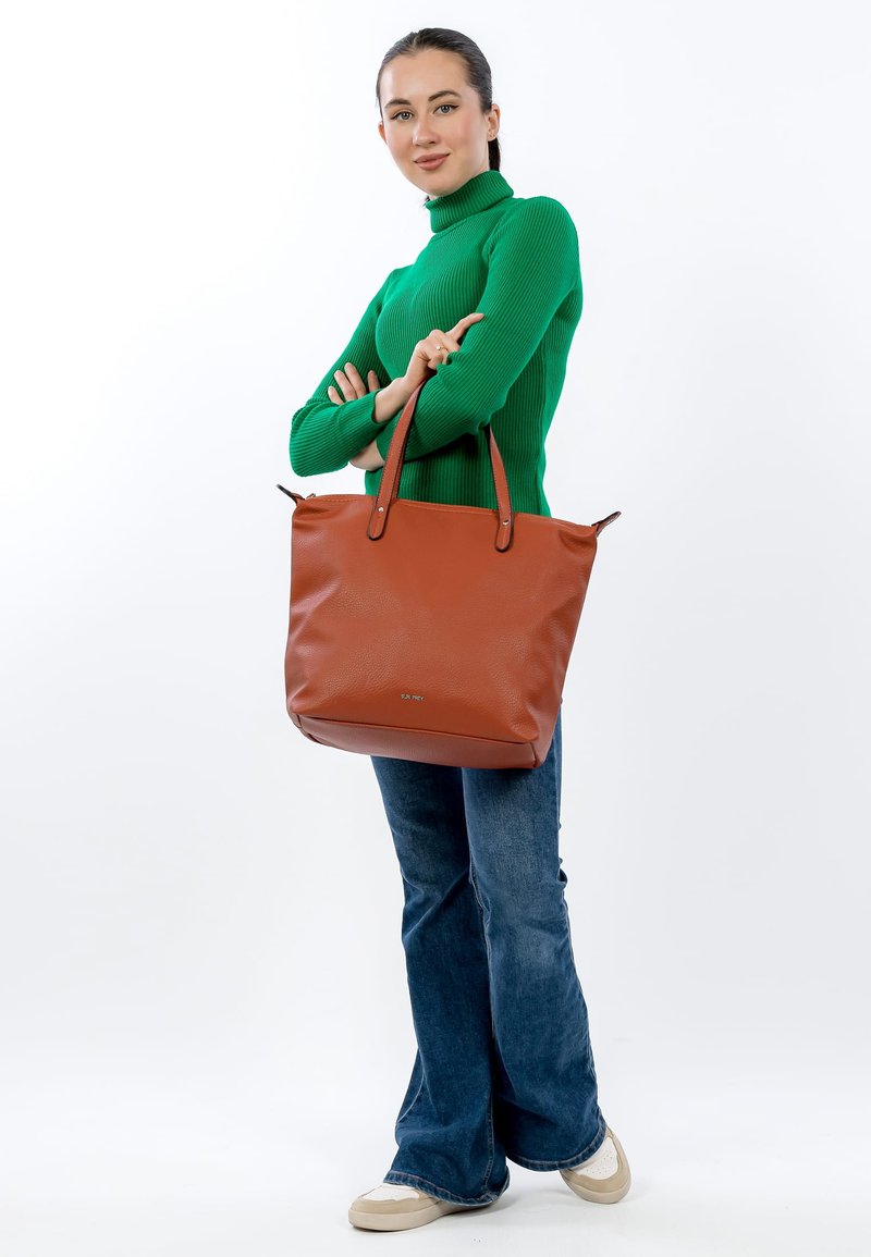 Brown leather tote bag with two handle straps and a soft texture. Worn with blue flared jeans and cream sneakers. Green ribbed sweater.