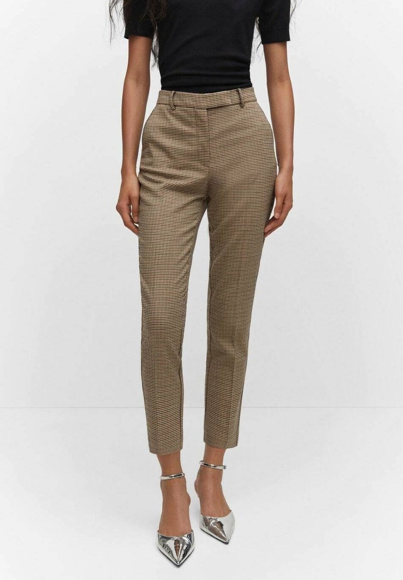 Femme portant un pantalon slim taille haute à carreaux marron, associé à un haut noir à manches courtes et des talons argentés à bride cheville pointue.