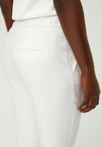 White trousers with a smooth texture, elastic waistband, and a single back pocket. Side seams are seamless for a clean look.